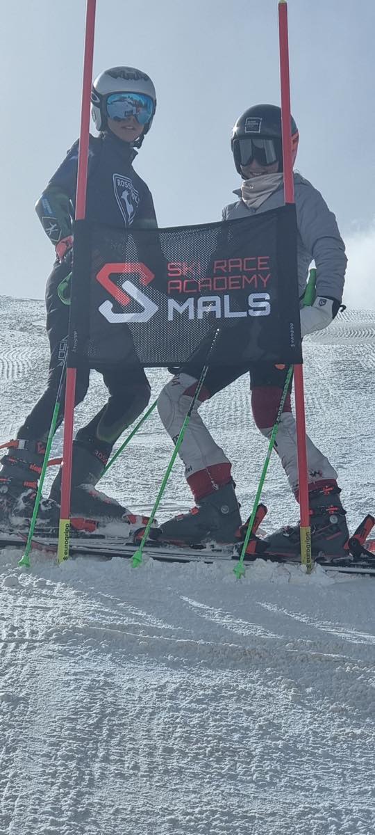 Two Ski Race Academy Mals athletes holding the academy banner between race gates